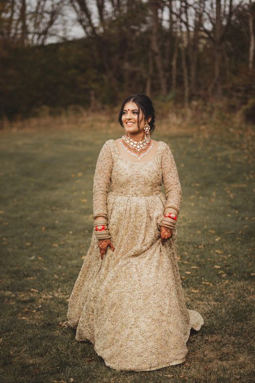 Bride smiling in field wearing gold long dress