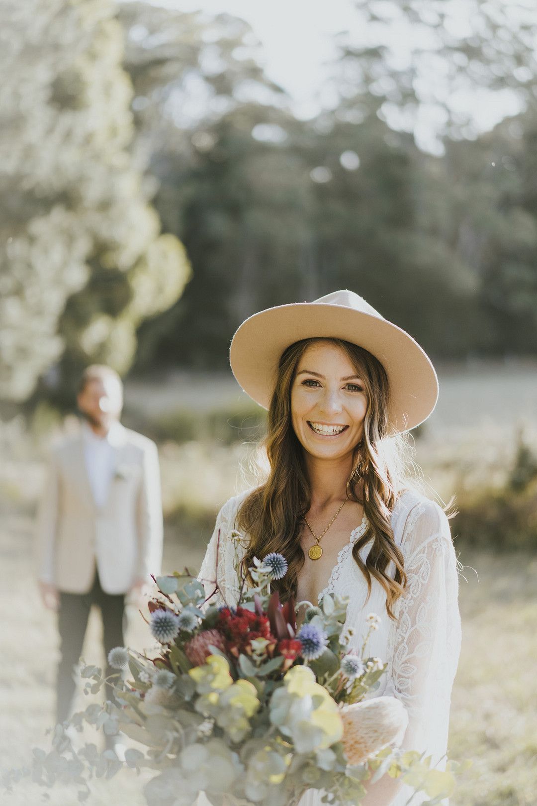 rustic bride wearing felt hat with groom in the distance