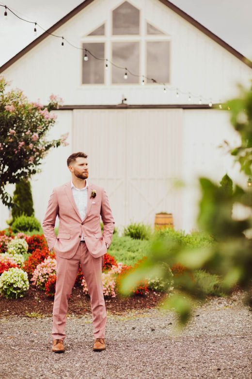 Groom in pink suit standing in front of barn wedding venue