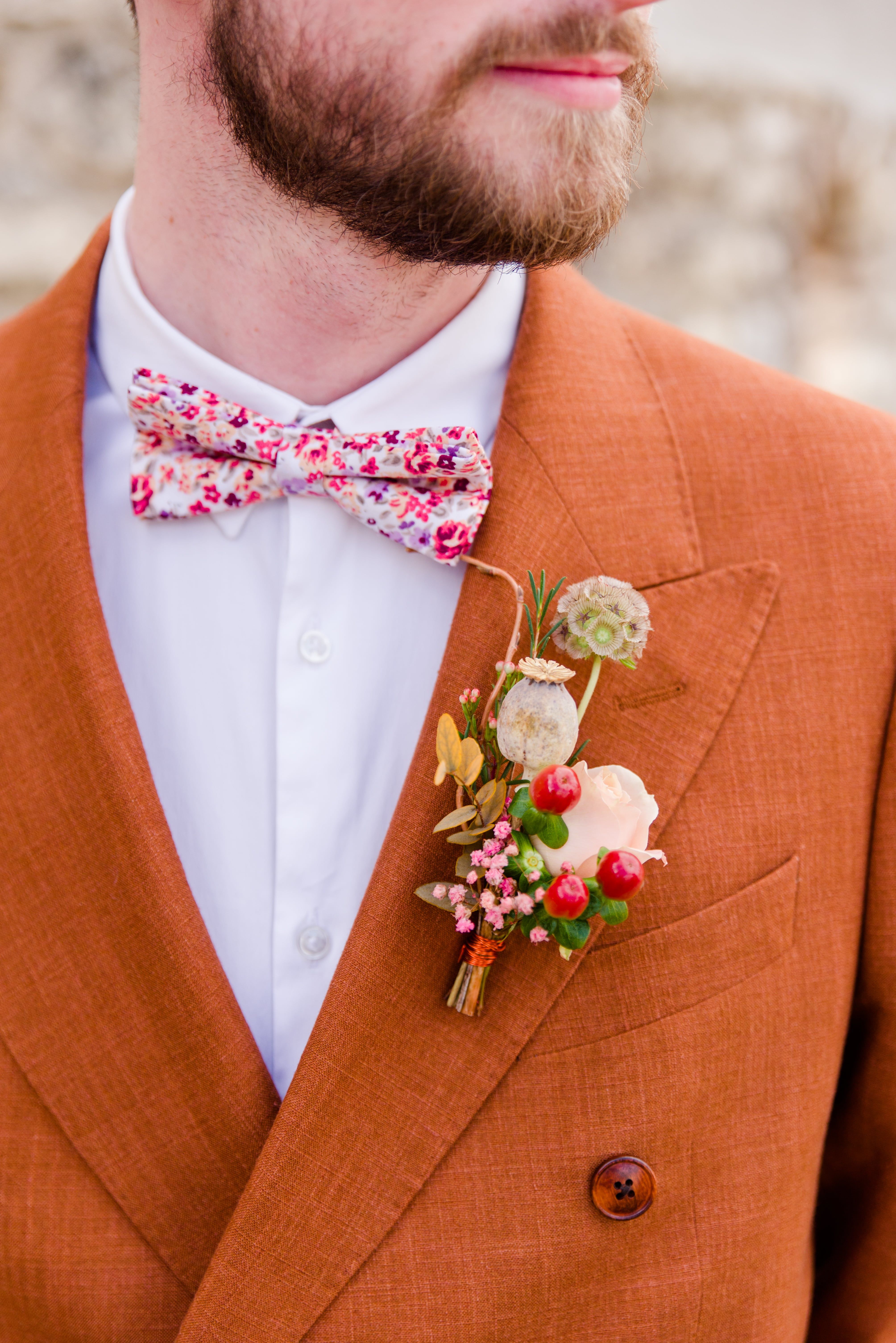 Groom wearing terracotta colored suit with dried flower boutonniere