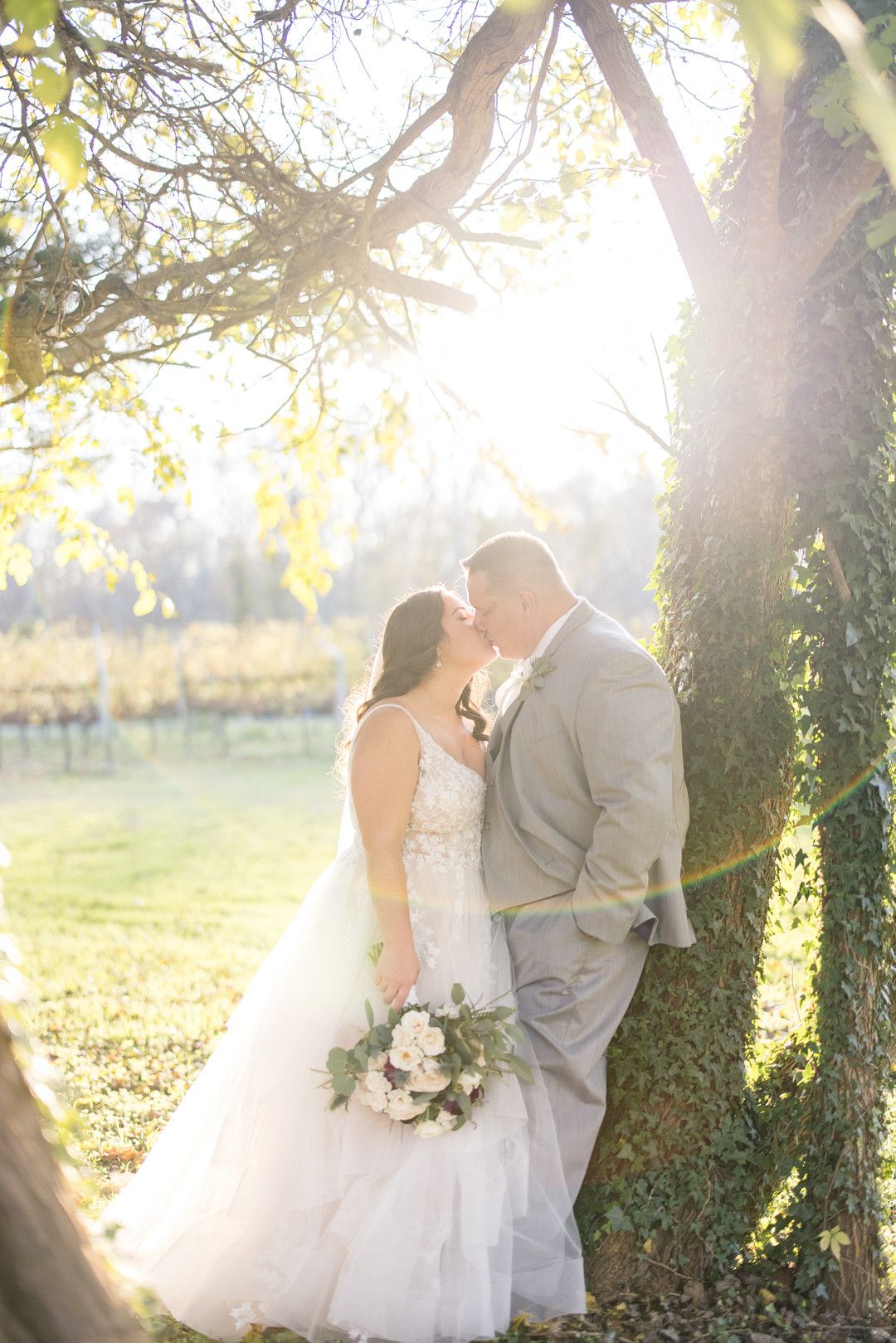 bride and groom leaning against tree kissing