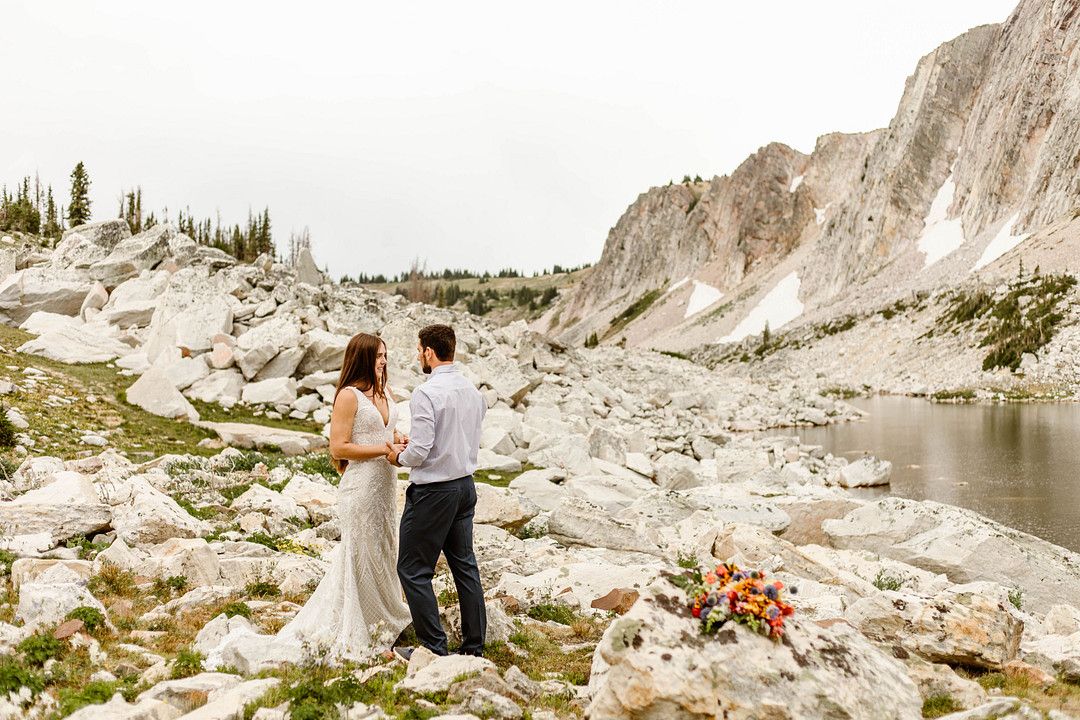 bride and groom holding hands next to lake and mountains