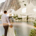 bride and groom looking over a mountain with a rainbow