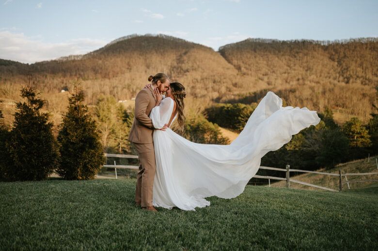 bride and groom kissing on hillside, bride dress blowing in the wind