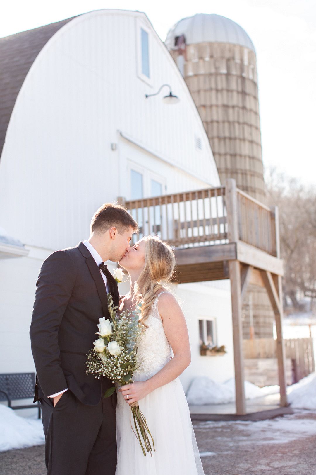 bride and groom kissing in front of white barn 