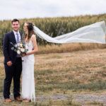 bride and groom standing next to each other with the bride's veil blowing in the wind