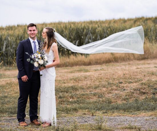 bride and groom standing next to each other with the bride's veil blowing in the wind