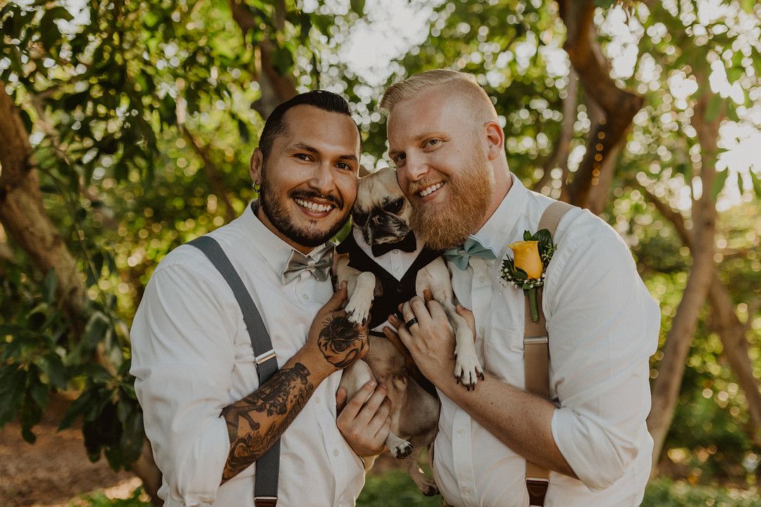 grooms holding a dog at their wedding