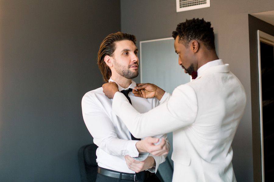groom helping other groom with his tie at at-home wedding