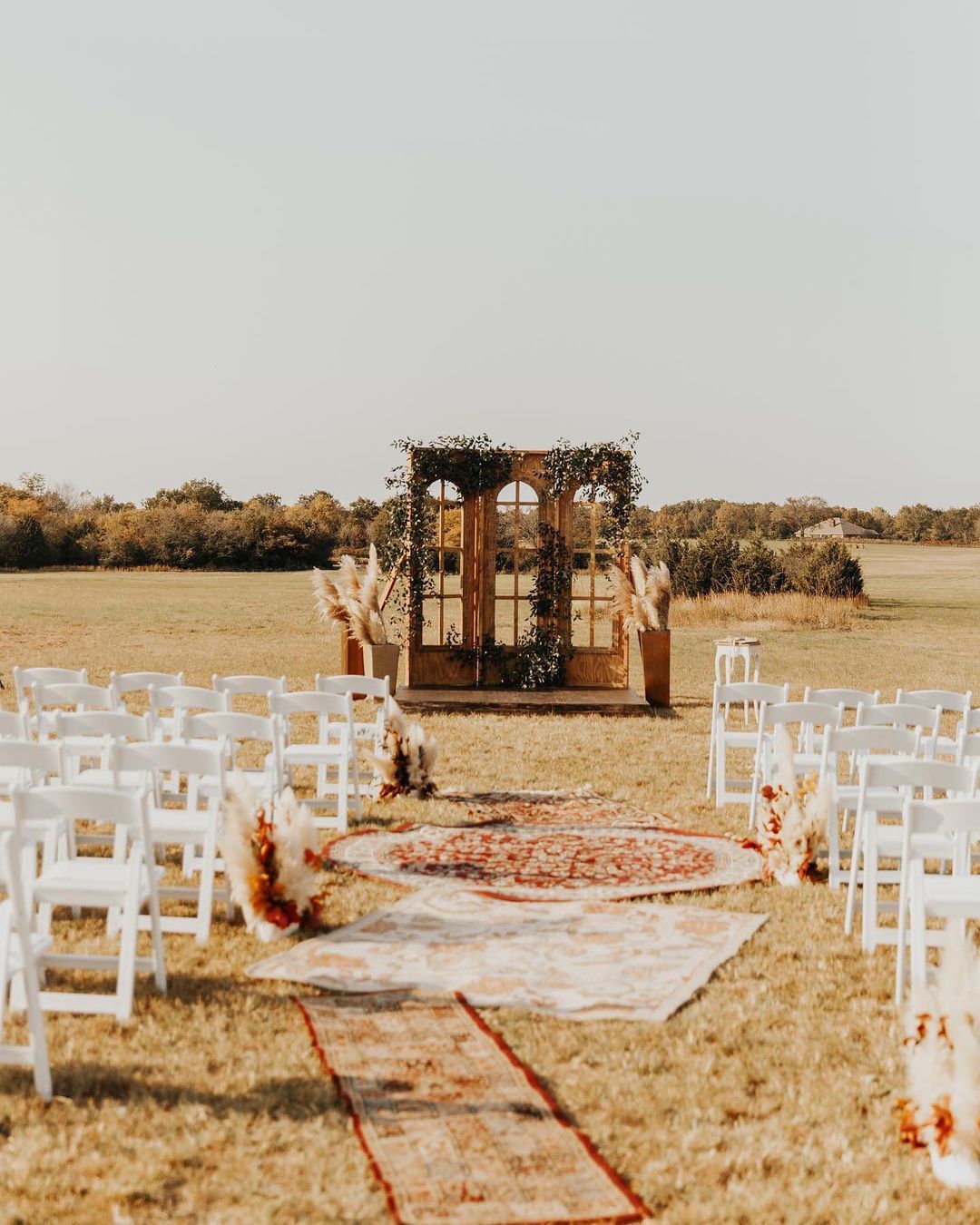 an outdoor wedding aisle with vintage rugs and a rustic door as the ceremony alter