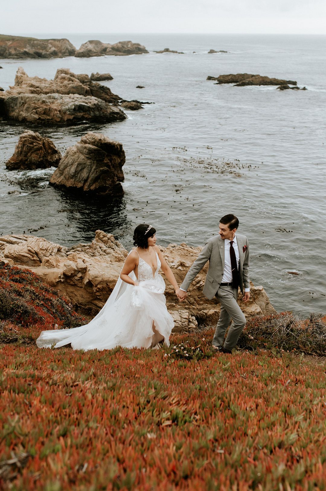 Bride and groom walking along cliff in a coastal wedding in Big Sur, California