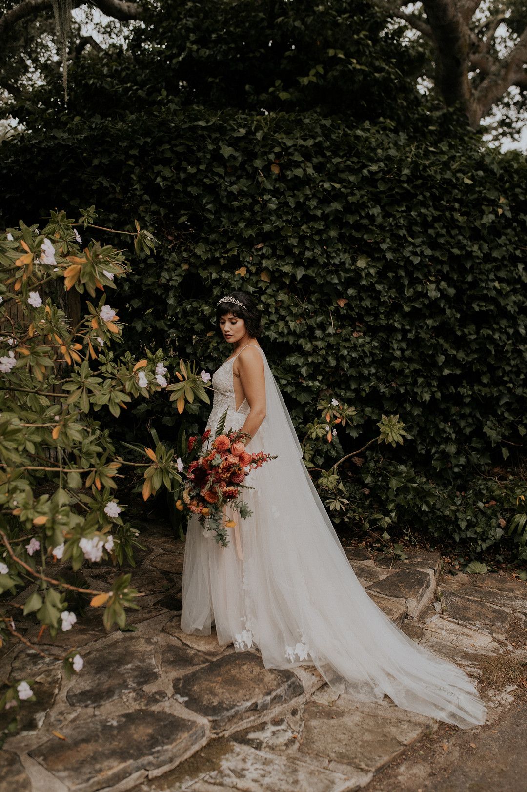 bride posing with flowers in front of greenery