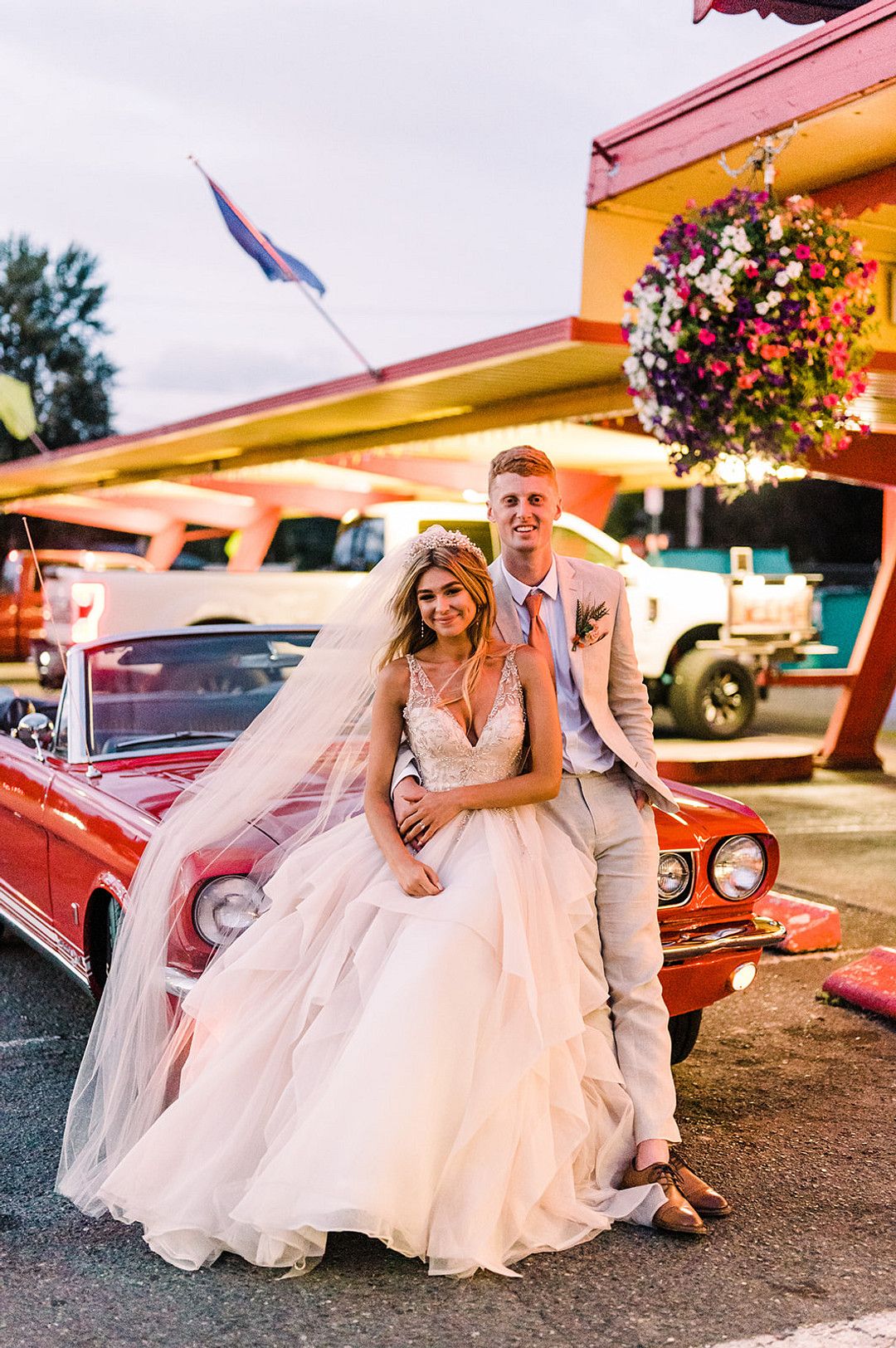 bride and groom leaning on red convertible
